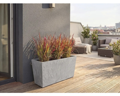 Jardinière rectangulaire grise aspect pierre avec herbe ornementale sur une terrasse de toit avec plancher en bois et meubles de salon.