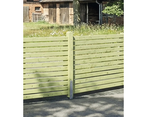 Horizontaler Holzzaun aus Lamellen mit Pfosten und Metallanker vor einer ländlichen Gartenkulisse.