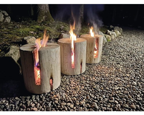 Drei brennende Schwedenfeuer aus Holz auf einem Kieselweg im Außenbereich bei Nacht mit Bäumen im Hintergrund.