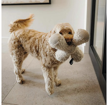 Chien avec un grand jouet en peluche pour chien en forme d'os dans la gueule sur un sol carrelé.