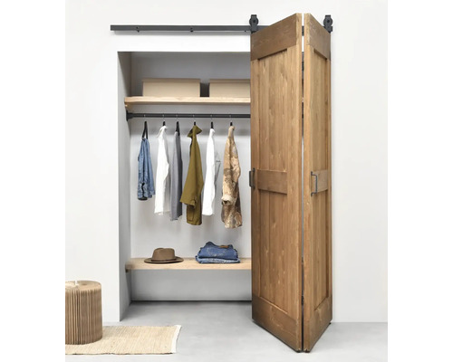 Zweiflügelige Schiebetür aus Holz im Scheunentor-Stil vor einem organisierten Kleiderschrank mit schwarzem Schienensystem.