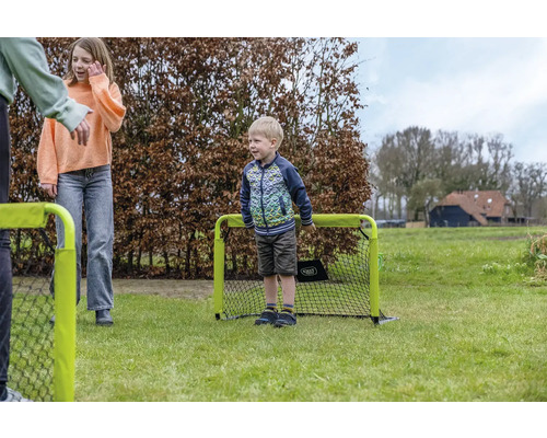 Enfants jouant avec un petit but de football portable sur une pelouse dans le jardin.