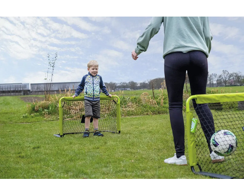 Un enfant et un adulte jouent au football dans le jardin avec deux petits buts de foot verts sur une pelouse.