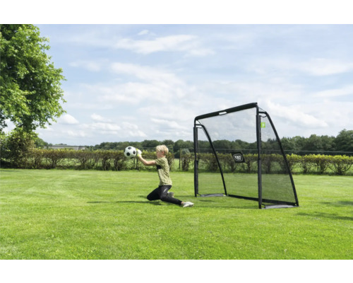 Un enfant attrape un ballon de football devant un but de foot noir sur une pelouse verte dans un jardin clair et ensoleillé.