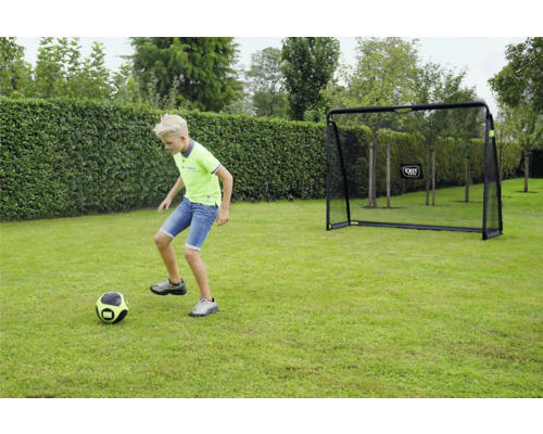 Un enfant joue au football sur une pelouse devant un but de football EXIT Toys dans un jardin.