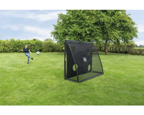 Une fille joue au football avec un filet de rebond EXIT Toys noir doté d une paroi de tir dans un jardin.