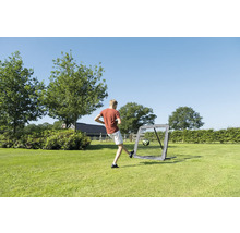 Person schießt Fußball gegen ein Rebounder-Netz in einem weitläufigen Garten mit Bäumen unter freiem Himmel.