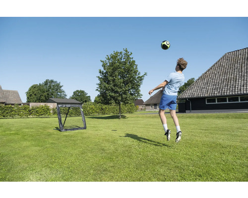 Ein Junge spielt Fußball auf einem grünen Rasen mit einem schwarzen tragbaren Fußballtor in einem weitläufigen Garten.