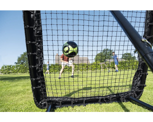 Fußball Rebounder Netz am Gaart mat engem fliegenden Fußball a spillenden Persounen op enger Wiss.