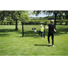 Deux enfants jouent au football avec un but de football EXIT Toys sur une pelouse dans un jardin clair et ensoleillé.
