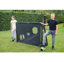 Deux enfants avec des ballons de foot à côté d un but de football noir EXIT Toys avec une paroi d entraînement à deux trous sur du gazon.