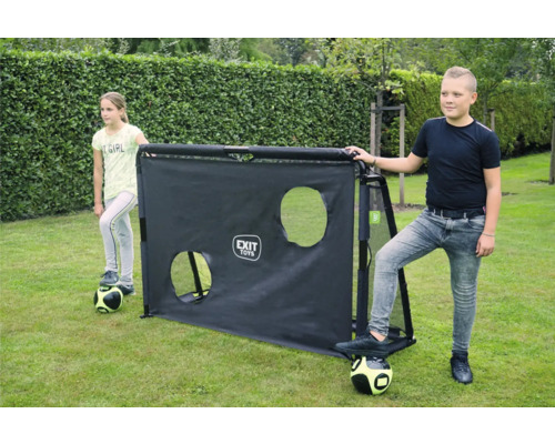 Deux enfants avec des ballons de foot à côté d un but de football noir EXIT Toys avec une paroi d entraînement à deux trous sur du gazon.