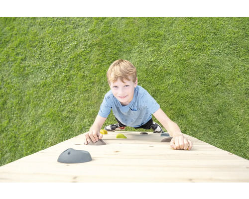 Un enfant grimpe sur un mur d escalade en bois avec des prises colorées sur une pelouse.