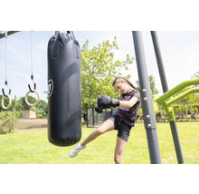 Ein Mädchen trainiert mit einem Boxsack an einer Outdoor-Spielstation in einem hellen Garten mit Turnringen.