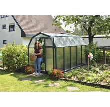 Garten-Gewächshaus mit dunkelgrünem Rahmen, Scheunenform und lichtdurchlässigen Paneelen, eine Frau mit Korb steht in der offenen Tür.