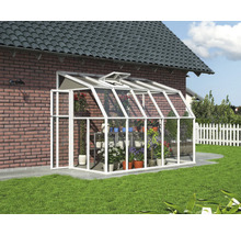 Weißes Anlehn-Gewächshaus mit Glaswänden an einer Backsteinmauer, gefüllt mit Topfpflanzen auf einem Rasen im Garten.