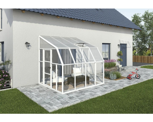 Anlehngewächshaus aus Aluminium in Weiß mit Verglasung, an einer Hauswand auf einer gepflasterten Terrasse montiert, mit Dachfenster und Tür.
