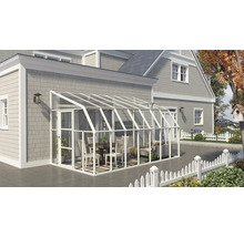 Weißer Anlehn-Wintergarten aus Aluminium und Glas an einem grauen Haus. Innenraum mit Holzmöbeln und Sofa auf einer gefliesten Terrasse.