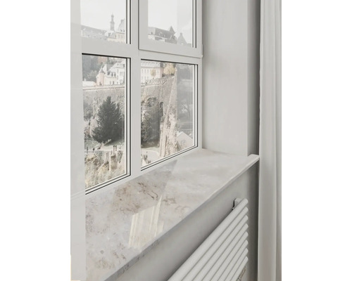 Appui de fenêtre clair aspect pierre naturelle sous un cadre de fenêtre blanc avec vue sur des murs historiques.