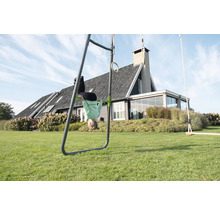 Portique de jeux en métal dans un jardin avec barre de traction, anneaux de gymnastique et balançoire, enfant la tête en bas devant une maison.