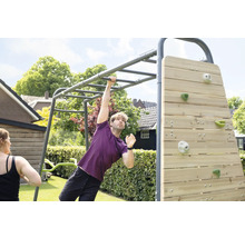 Un homme s entraîne sur une structure de fitness extérieure en métal gris avec une échelle de suspension et un mur d escalade en bois.