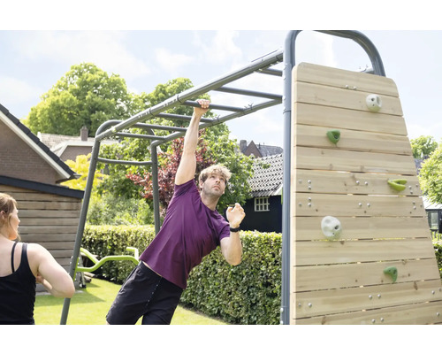 Un homme s entraîne sur une structure de fitness extérieure en métal gris avec une échelle de suspension et un mur d escalade en bois.