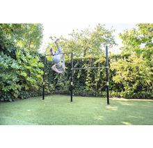 Barre de gymnastique double en métal dans le jardin, un enfant fait de la gymnastique la tête en bas, entouré de haies, atmosphère claire.