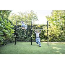 Deux enfants jouent sur une double barre de gymnastique en métal dans un jardin sur une pelouse.