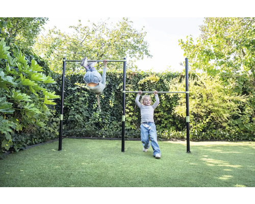 Deux enfants jouent sur une double barre de gymnastique en métal dans un jardin sur une pelouse.