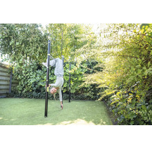 Un enfant fait de la gymnastique sur une barre fixe en métal noir dans un jardin vert et lumineux avec gazon synthétique.