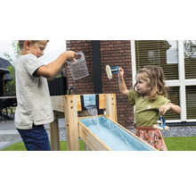 Deux enfants jouent avec un circuit d'eau en bois dans le jardin. Un garçon verse de l'eau, une fille joue avec des petits radeaux en bois.