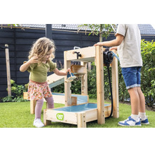 Des enfants jouent dans un jardin avec un circuit d eau EXIT Toys en bois, équipé d une pompe à eau et de plusieurs niveaux sur du gazon vert.