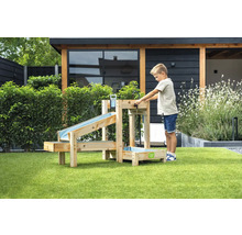 Enfant joue dans le jardin avec un circuit d'eau en bois à plusieurs niveaux et des bassins de récupération sur une pelouse devant un abri de jardin.