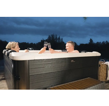 Un couple se détend dans un jacuzzi MSpa rectangulaire avec un habillage extérieur aspect bois foncé dans le jardin au crépuscule.