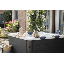 Un couple se détend dans un jacuzzi extérieur rectangulaire moderne avec un habillage aspect bois sombre dans un jardin fleuri.