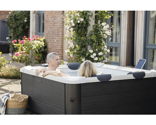 Un couple se détend dans un jacuzzi extérieur rectangulaire moderne avec un habillage aspect bois sombre dans un jardin fleuri.