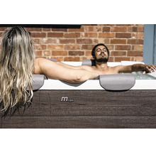 Un homme et une femme se détendent dans un jacuzzi MSpa avec un habillage aspect bois devant un mur de briques.