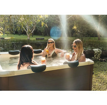 Trois femmes se détendent dans un jacuzzi extérieur rectangulaire avec appuie-tête dans un jardin près d'un étang.