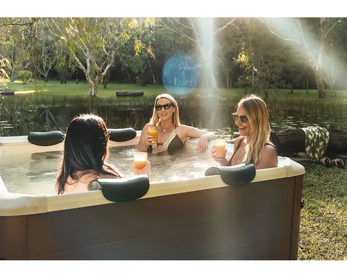 Trois femmes se détendent dans un jacuzzi extérieur rectangulaire avec appuie-tête dans un jardin près d'un étang.