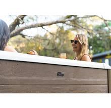 Vue extérieure d'un jacuzzi MSpa avec panneaux aspect bois et personnes dans un jardin.