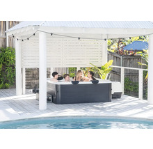 Famille dans un jacuzzi sous un pavillon clair sur une terrasse en bois au bord de la piscine avec guirlande lumineuse.