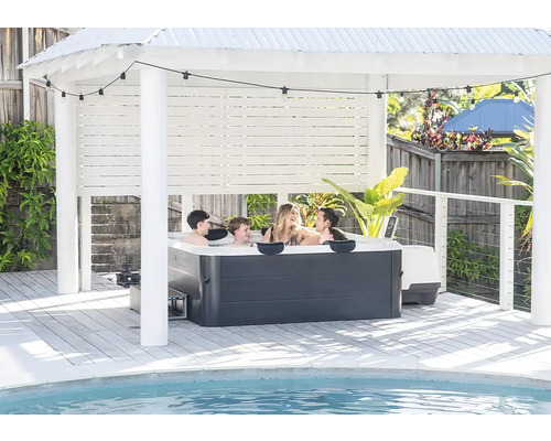 Famille dans un jacuzzi sous un pavillon clair sur une terrasse en bois au bord de la piscine avec guirlande lumineuse.