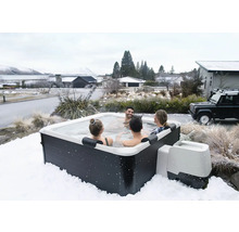 Spa extérieur carré avec quatre personnes dans un paysage hivernal enneigé, habillage sombre et coque intérieure blanche.