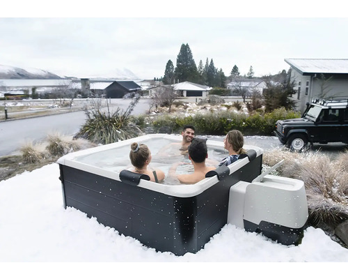 Spa extérieur carré avec quatre personnes dans un paysage hivernal enneigé, habillage sombre et coque intérieure blanche.