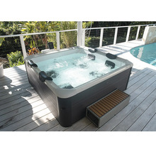 Jacuzzi extérieur avec habillage gris foncé et coque intérieure blanche, appuie-tête et eau bouillonnante sur une terrasse en bois.