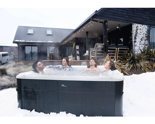 Quatre personnes se relaxent dans un spa extérieur MSpa dans un paysage enneigé devant une maison moderne en bois.