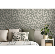 Vliestapete mit botanischem Blättermuster im Schlafzimmer hinter einem Bett mit Kissen und einer Zimmerpflanze auf einem Beistelltisch.
