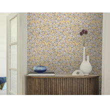 Espace de vie avec papier peint à motif de feuilles, buffet en bois, vase blanc et bol en verre bleu.