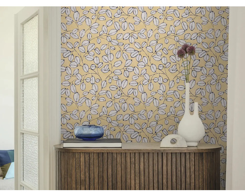 Espace de vie avec papier peint à motif de feuilles, buffet en bois, vase blanc et bol en verre bleu.