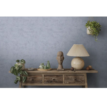 Buffet rustique en bois devant un mur bleu-gris texturé avec une lampe de table, une sculpture en pierre, des bouteilles en verre et des plantes.
